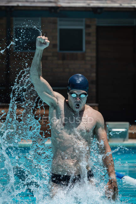 Фронтальний вид молодих кавказьких чоловіків плавець святкувати перемогу і підвищення кулаком у відкритому басейні на сонці — стокове фото