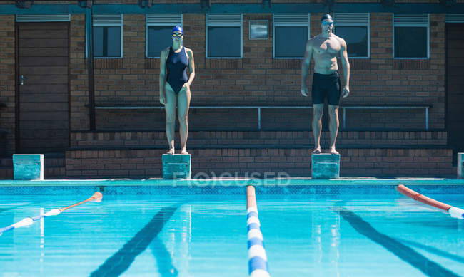 Vista frontal de nadadores caucasianos masculinos e femininos que se encontram nos blocos iniciais da piscina — Fotografia de Stock