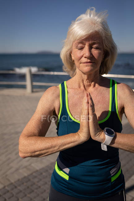 Вид спереди активной пожилой женщины, занимающейся йогой на набережной под солнцем — стоковое фото