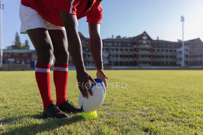 Sección baja de un jugador de rugby masculino que se prepara para patear la pelota en el campo de rugby en un día soleado - foto de stock