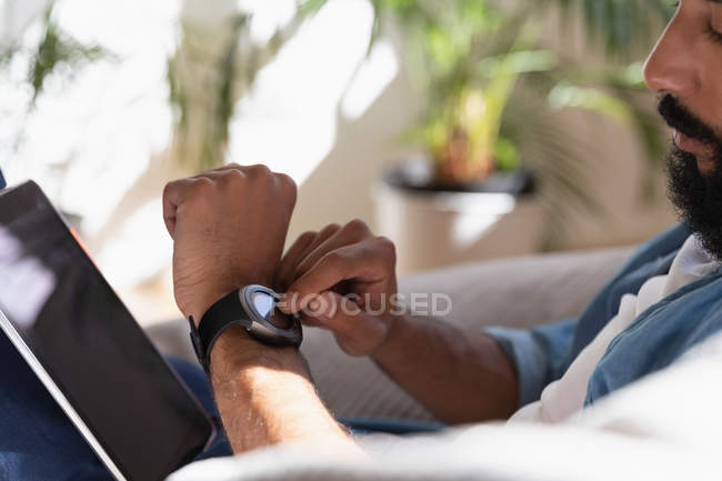 Vista lateral do homem afro-americano usando relógio inteligente em casa — Fotografia de Stock