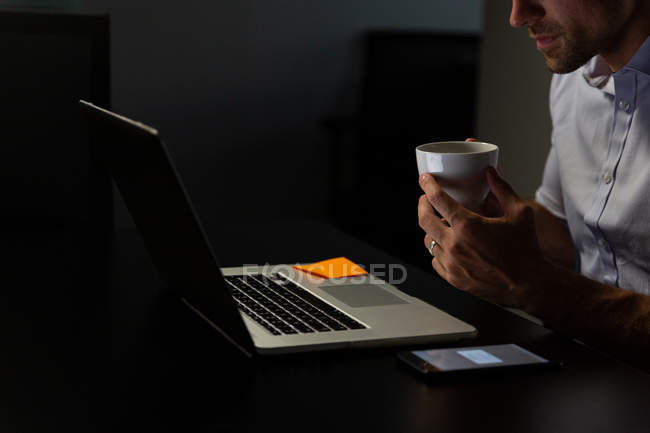 Mid section of young male executive having coffee while working on laptop at table in a modern office — Stock Photo