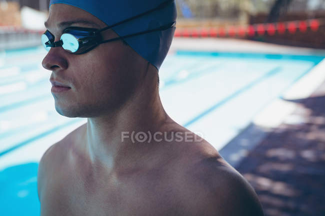 Close-up vista lateral do jovem nadador caucasiano masculino com óculos de natação em pé na piscina — Fotografia de Stock