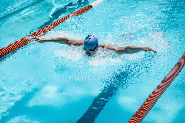 Vue en angle élevé du jeune nageur masculin caucasien nageant coup de papillon dans la piscine extérieure le jour ensoleillé — Photo de stock