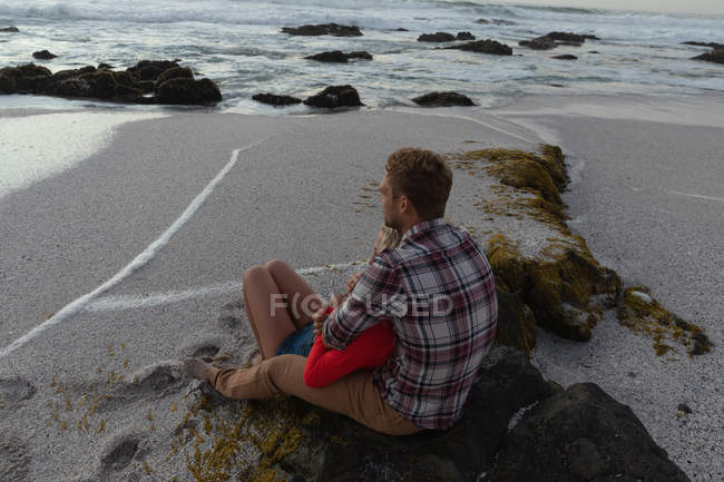 Vista de ángulo alto de la joven pareja romántica sentada en la playa. Se abrazan. - foto de stock
