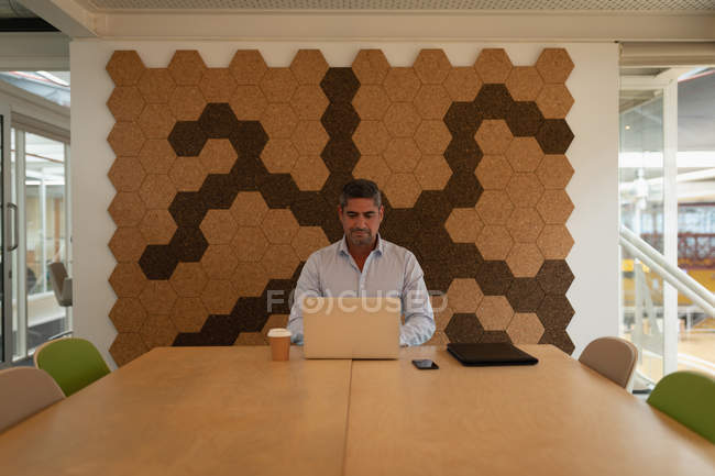 Vue de face d'un homme d'affaires travaillant sur son ordinateur portable et assis au bureau — Photo de stock