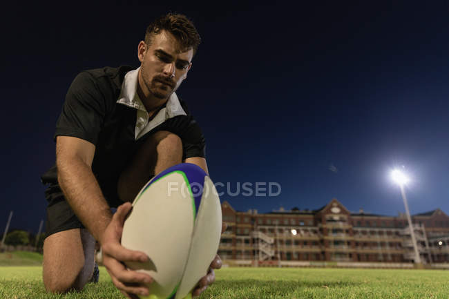 Vue à angle bas du joueur de rugby plaçant la balle de rugby sur le tee-shirt de coups de pied dans le stade la nuit — Photo de stock