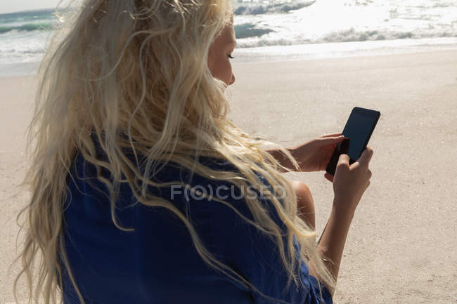 Side view of beautiful blonde woman using mobile phone at beach on a sunny day — Stock Photo