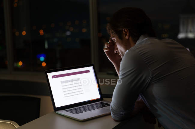 Vista lateral de belo jovem executivo do sexo masculino trabalhando em laptop na mesa em um escritório moderno — Fotografia de Stock