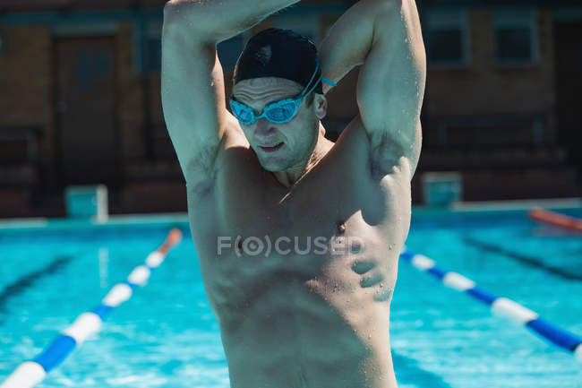 Vista frontal de um jovem nadador masculino com óculos de natação esticados na piscina — Fotografia de Stock