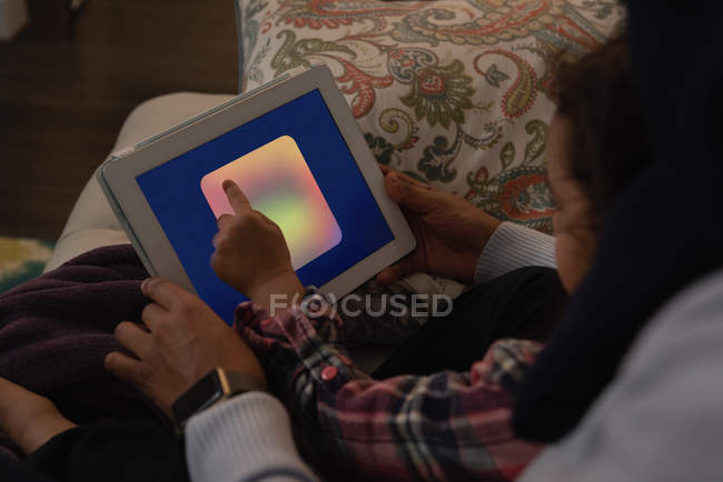 Високий кут зору змішаної раси мати і дочка, використовуючи цифровий планшет вдома на дивані у вітальні — стокове фото