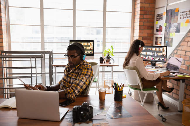 Вид спереду на різних бізнесменів, що працюють в офісі над ноутбуком та навушниками — стокове фото