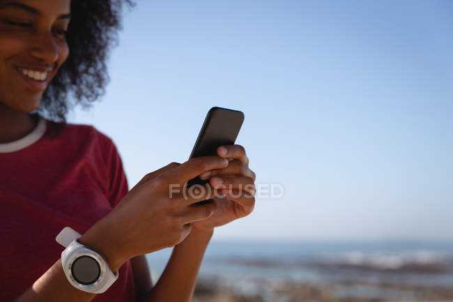 Gros plan de la belle femme afro-américaine utilisant un téléphone portable à la plage le jour ensoleillé — Photo de stock
