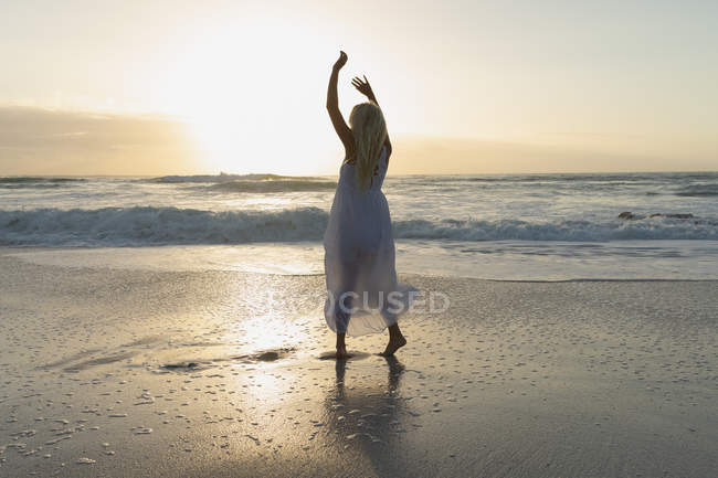 Вид спереду молода жінка позує, стоячи на пляжі в сонячний день. Вона насолоджується заходом сонця — стокове фото