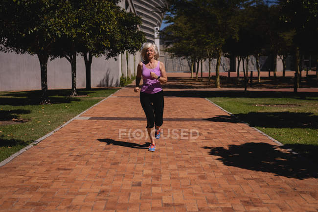 Вид спереди активной пожилой женщины, делающей пробежку в парке в солнечный день — стоковое фото