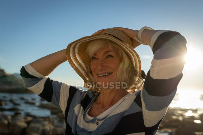 Vista frontal de una mujer mayor activa sonriendo y de pie en la playa - foto de stock