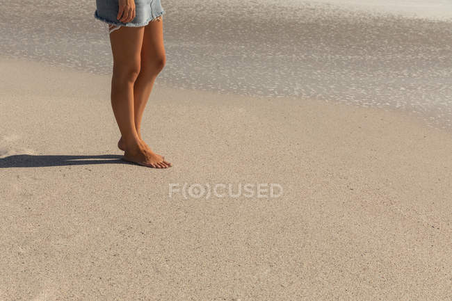 Bassa sezione di donna caucasica abbronzata in piedi sulla spiaggia in una giornata di sole. Sta camminando. — Foto stock
