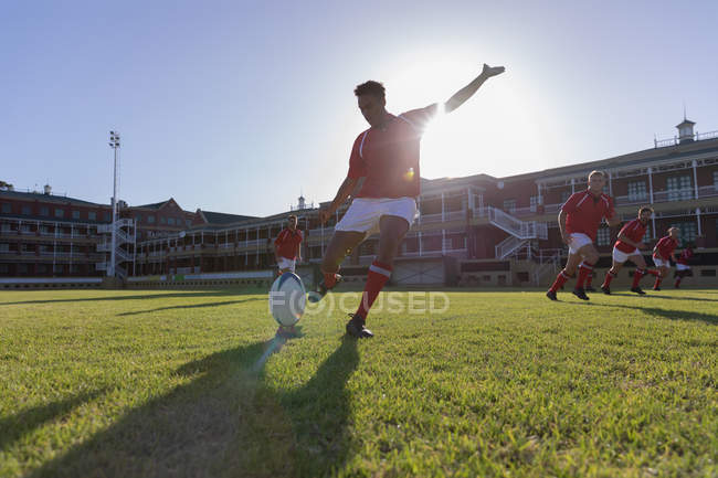 Front view of a male African american rugby player kicking the ball from the kicking tee in the stadium on a sunny day — Stock Photo