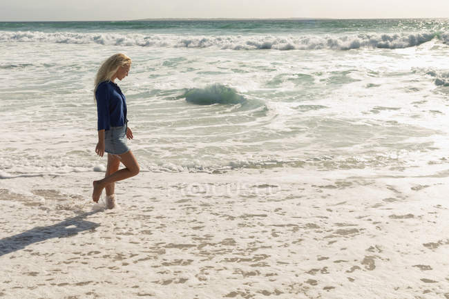 Side view of blonde woman walking at beach on a sunny day. She is walking — Stock Photo