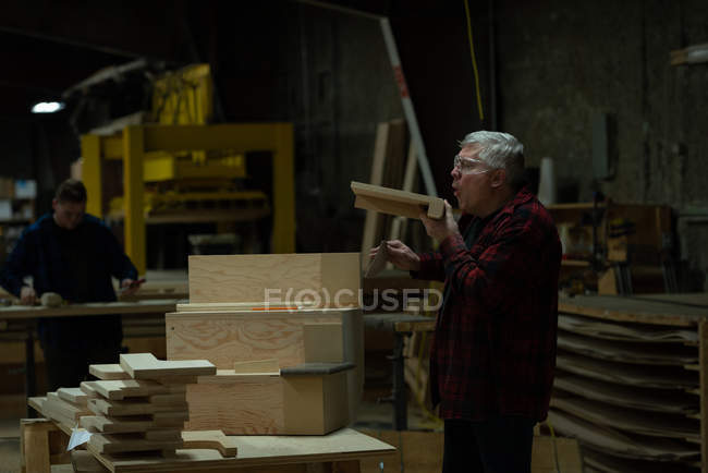 Vista lateral del carpintero soplando polvo de sierra de madera en el taller - foto de stock