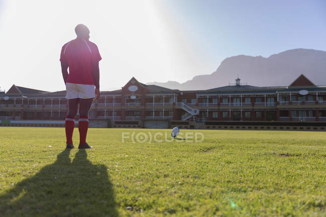 Vista trasera de un jugador de rugby afroamericano que espera para patear la pelota de rugby en el campo de rugby - foto de stock