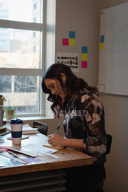 Вид сбоку на предпринимательницу, сидящую и пишущую на блокноте в офисе — стоковое фото