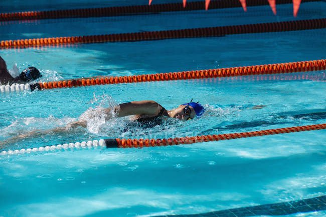 Vista laterale di giovani nuotatrici che nuotano strisciando in piscina in una giornata di sole — Foto stock