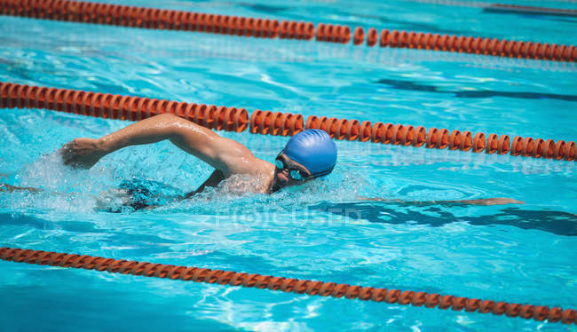 Vista lateral do jovem nadador masculino caucasiano nadando estilo livre na piscina no dia ensolarado — Fotografia de Stock