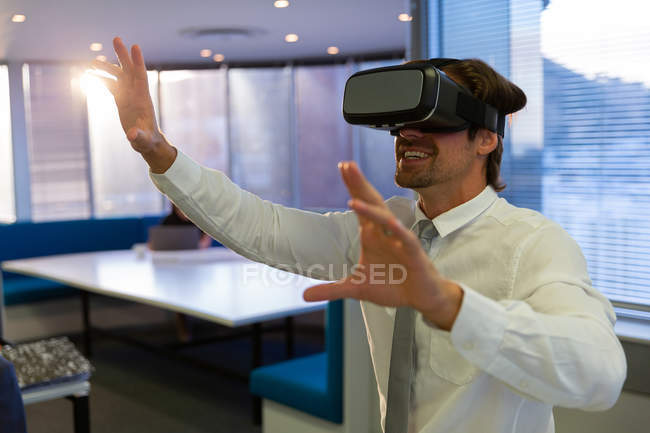 Vista frontal do jovem executivo feliz usando fone de ouvido realidade virtual em um escritório moderno — Fotografia de Stock