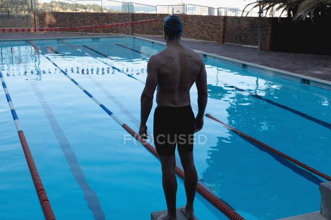 Visão traseira de um nadador caucasiano macho em pé em um bloco inicial e olhando para a piscina — Fotografia de Stock