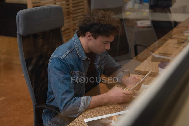 Vista lateral de hombre de negocios de raza mixta vestido casualmente usando tableta digital mientras está sentado en la oficina - foto de stock