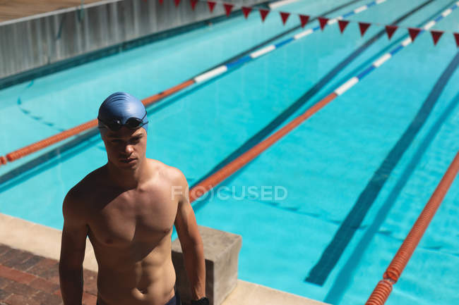 Vue en angle élevé du jeune nageur masculin caucasien regardant concentré tout en se tenant à la piscine extérieure le jour ensoleillé — Photo de stock