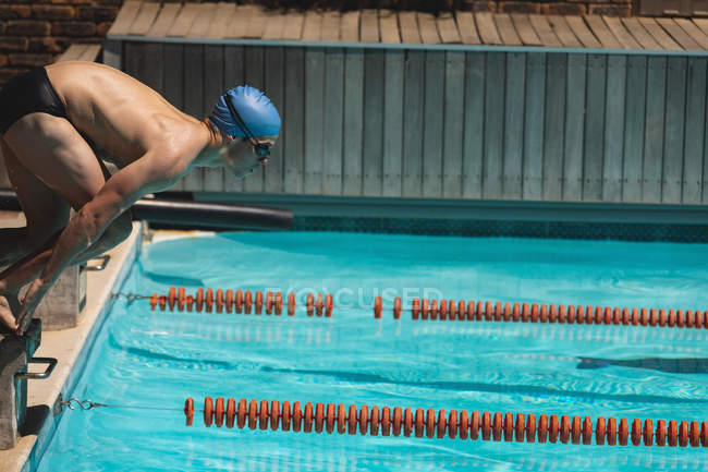 Vista lateral de un joven nadador caucásico saltando al agua de una piscina al aire libre bajo el sol - foto de stock