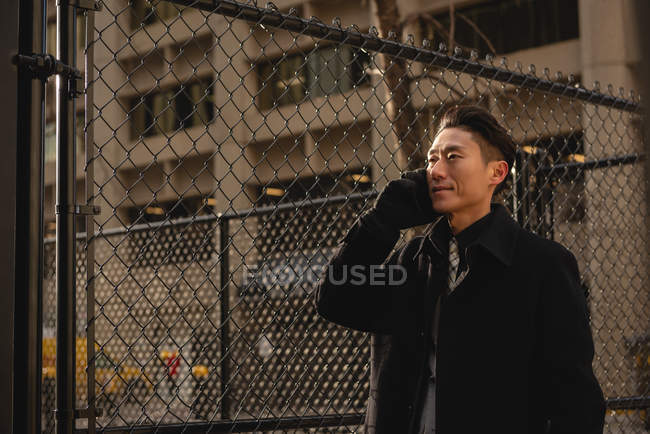 Vista lateral de belo jovem empresário asiático falando no telefone celular na rua na cidade — Fotografia de Stock