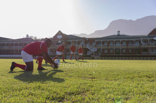 Side view of a male African american rugby player placing the rugby ball on a kicking tee in the rugby playground on a sunny day — Stock Photo