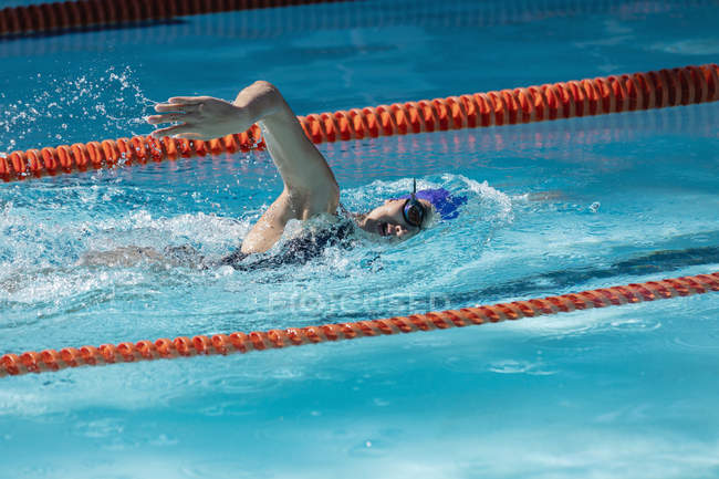 Side view of a young female swimmer swimming freestyle crawl in the swimming pool on a sunny day — Stock Photo