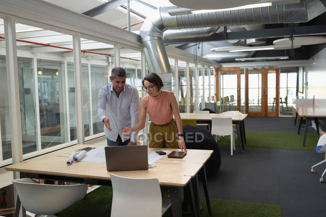 Вид спереди многоэтнических бизнесменов, стоящих в офисе и обсуждающих за синим принтом на столе — стоковое фото
