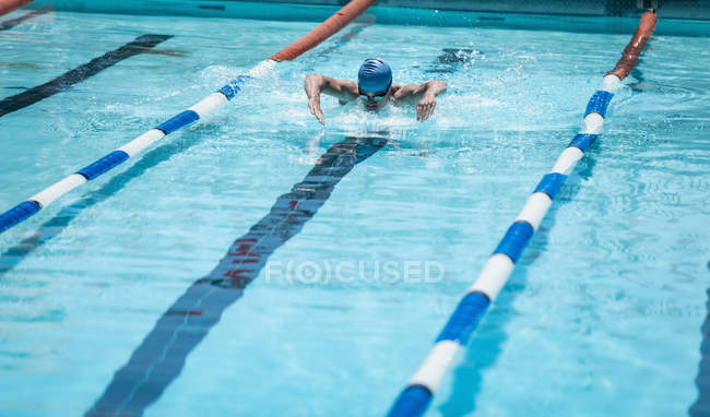 Vue de face du jeune nageur masculin caucasien nageant course de papillon dans la piscine le jour ensoleillé — Photo de stock