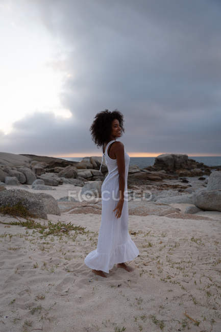 Seitenansicht einer afrikanisch-amerikanischen Frau, die in der Abenddämmerung auf einem Zobel am Meer tanzt und genießt — Stockfoto
