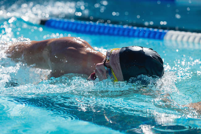 Vista frontal de um jovem nadador masculino nadando rastejar na piscina em um dia ensolarado — Fotografia de Stock