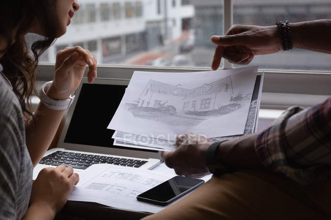 Close up of diverse business people discussing over blueprint in office at desk — Stock Photo