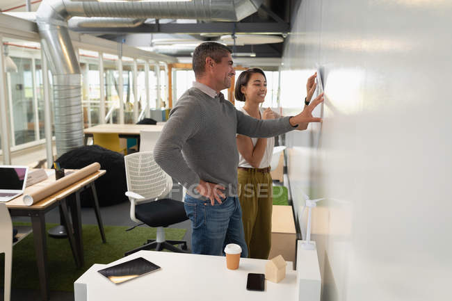 Side view of multi ethnic business people discussing over a blueprint against a wall in the office — Stock Photo