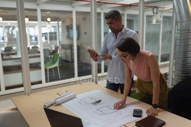 Вид сбоку многоэтнических бизнесменов, работающих над цифровым планшетом и синим принтом, стоя в офисе — стоковое фото