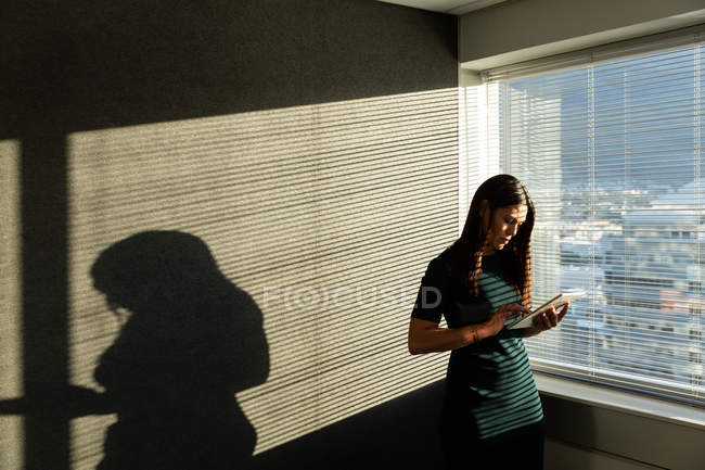 Vista frontal de uma jovem executiva trabalhando em tablet digital perto da janela em um escritório moderno — Fotografia de Stock