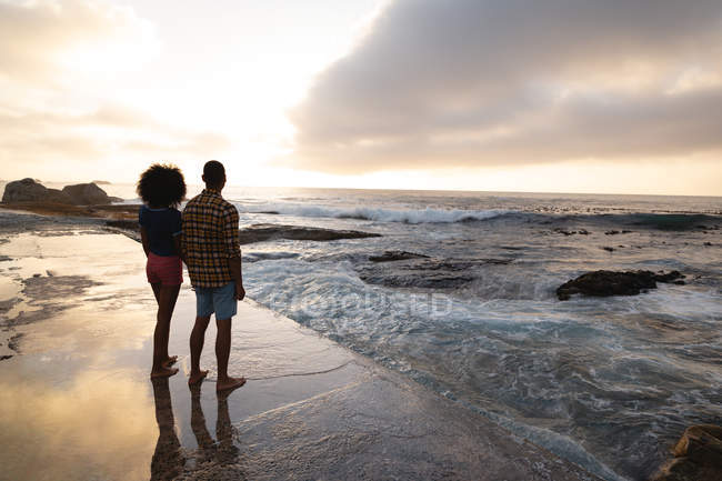Vista posteriore della coppia afro-americana in piedi sulla roccia vicino al mare. Guardano all'orizzonte. — Foto stock