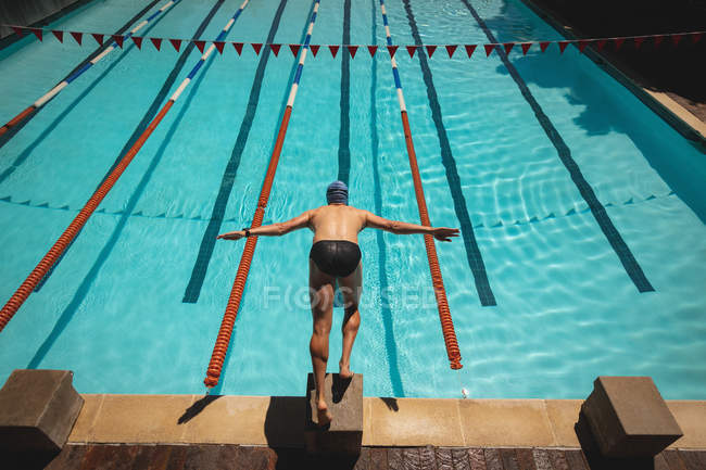 High angle view of young Caucasian male swimmer with arms stretched out jumping into water of a swimming pool on sunny day — Stock Photo
