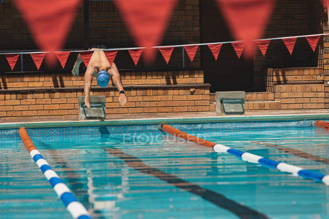 Vista frontale del giovane nuotatore maschio caucasico che si tuffa nell'acqua di una piscina sotto il sole — Foto stock