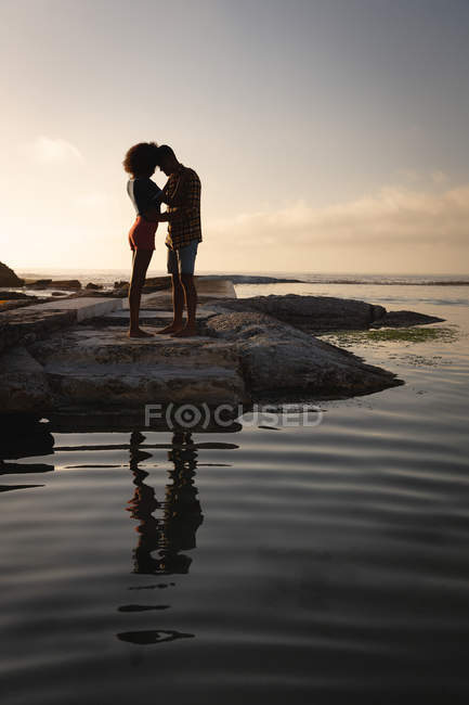 Vue de face du couple afro-américain debout dans l'humeur romantique près du bord de mer sur le rocher — Photo de stock