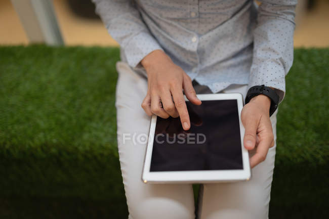 Mittelteil einer jungen Geschäftsfrau, die ein digitales Tablet berührt, während sie im Büro auf einer Bank aus Kunstrasen sitzt — Stockfoto