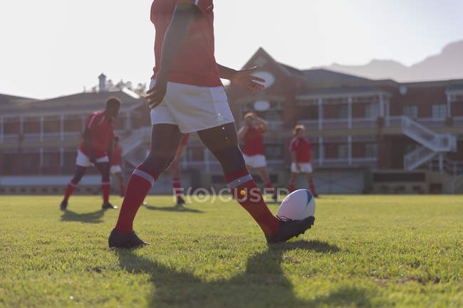 Sezione bassa di un giocatore di rugby afroamericano maschile che si prepara a calciare la palla nel terreno di rugby in una giornata di sole — Foto stock